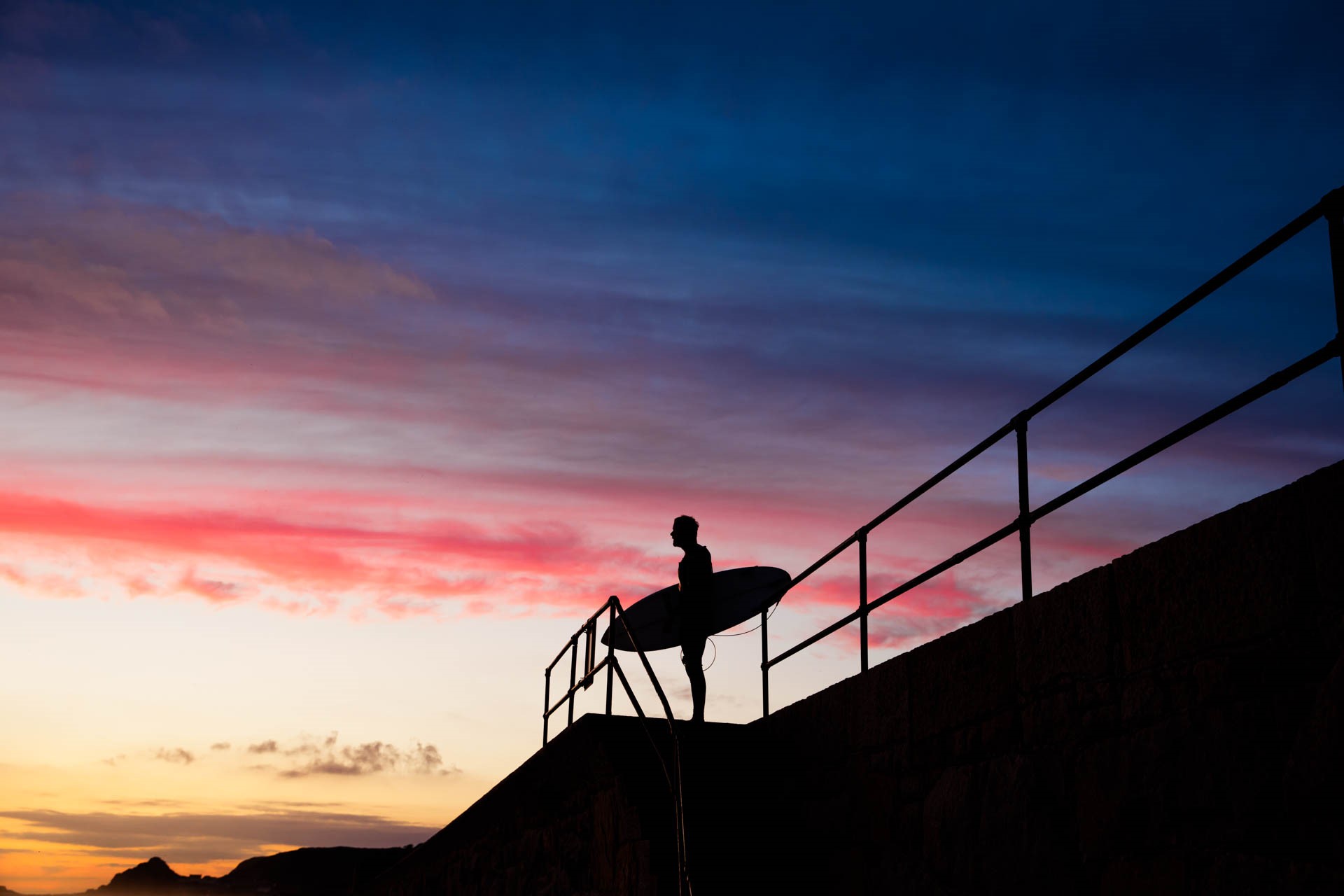 Surfer standing on seawall at St Ouen after Sunset